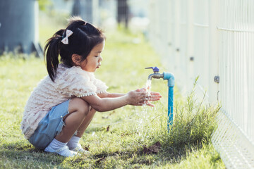 Cute 5 year old kid girl is washing her two hands from water tap. Child rubs hands together to wash her hands after playing at playground.