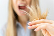 A shocked and upset blond woman holds the damaged brittle dry split ends of her long hair in her hand in front of her face, her mouth wide open in surprise, close-up. Health care and haircare concept.