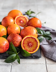 Wall Mural - Sliced and whole ripe juicy Sicilian blood oranges with leaves on black stone board, grey tiled background. Seasonal fruits.