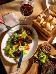 Wall Mural - Eating in restaurant with salad and wine glass on table background with woman hands 