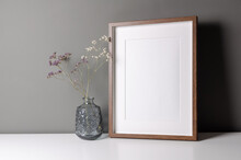 Vertical Wooden Frame Mockup For Artwork, Photo And Print Presentation On White Table Over Grey Wall, Dry Flowers In Vase.
