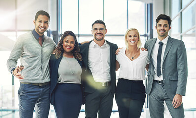 Our team knows no limits. Portrait of a diverse group of smiling coworkers standing arm in arm in an office.