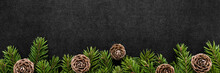 Dry Brown Cones And Green Fir Branches On Dark Black Table Background. Closeup. Christmas Natural Decorations. Empty Place For Inspirational Wishes Text, Quote Or Sayings. Wide Banner. Top Down View.