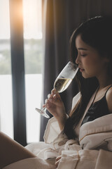 Beautiful asian woman wear bathrobe with glass of champagne at bedroom alcohol, celebration and drinking alone concept Asian sexy girl sit on bed at house or hotel room with holding champagne glass