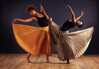 Practice and dedication make perfection. Two contemporary dancers with flowing skirts in front of a dark background.