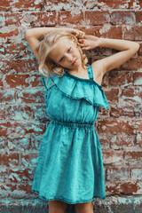 Wall Mural - a young blonde girl in a blue dress poses against a brick wall