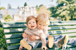 © annanahabed - Outdoor portrait of two adorable siblings resting on the bench in sunny park, preschooler brother hugging sweet toddler sister
