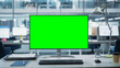 © Gorodenkoff - Desktop Computer Monitor with Mock Up Green Screen Chroma Key Display Standing on the Desk in the Modern Business Office. In the Background Glass Wall with Big City Office.