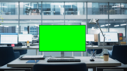 Wall Mural - Desktop Computer Monitor with Mock Up Green Screen Chroma Key Display Standing on the Desk in the Modern Business Office. In the Background Glass Wall with Big City Office.