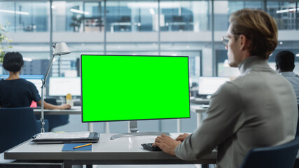 Leinwandbilder - Close Up Over the Shoulder Shot of a Businessman Working on Desktop Computer with Chroma Key Green Screen Mock Up Display. Digital Projects Manager Typing Data, Using Keyboard and Mouse.