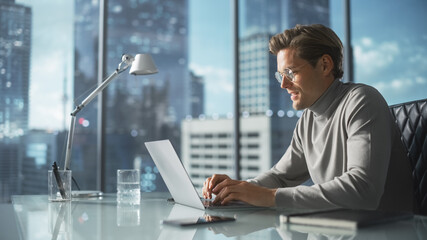 Poster - Creative Businessman in a Turtleneck Jumper Sitting in Modern Office, Using Laptop Computer Next to Window with Big City with Skyscrapers View. Successful Finance Manager Planning Work Projects.
