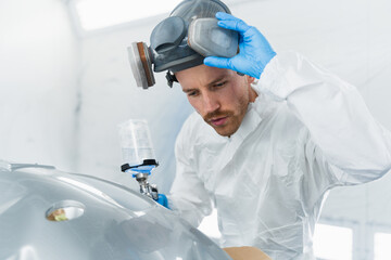 Wall Mural - Professional car painter in the painting booth takes off his protective mask to check the quality of the work done. Auto painter during work