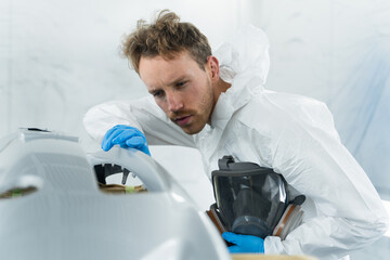 Wall Mural - Young car painter examines the surface of the car bumper in detail for the quality of the paintwork performed. Auto service employee works in the spray booth