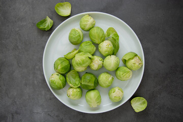 Fresh brussels sprouts in white plate isolated on dark background. Healthy vegan food, diet concept.