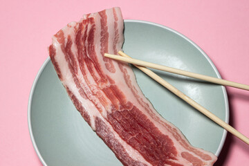 Canvas Print - Bacon on a pink background. Raw bacon on a plate. Chinese sticks next to pieces of meat. Pork meat