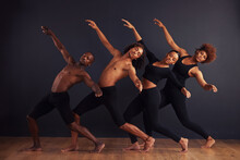 Perfectly Synchronised. A Group Of Dancers Performing A Dramatic Pose In Front Of A Dark Background.