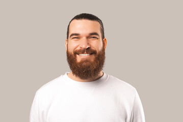 Wall Mural - Close up portrait of handsome young bearded hipster man looking at the camera and smiling over grey backdrop.