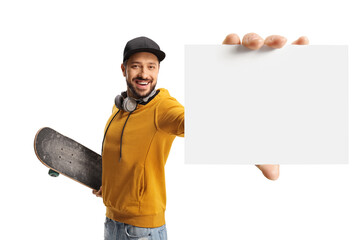 Poster - Cheerful guy in a yellow sweatshirt with a skateboard holding a blank cardboard