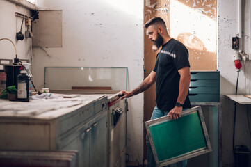 Wall Mural - Male worker using a screen exposure unit while working in a printing workshop