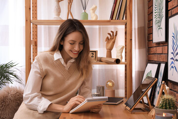 Poster - Young woman drawing in sketchbook with pencil at wooden table indoors