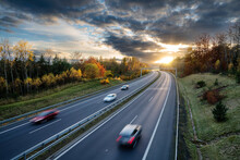 Motion Blurred Cars Driving On The Asphalt Highway In Forested Landscape In Autumn Colors At Sunset