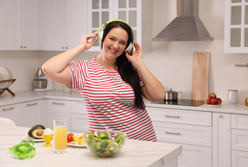 Canvas Print - Happy overweight woman with headphones dancing near table in kitchen. Healthy diet