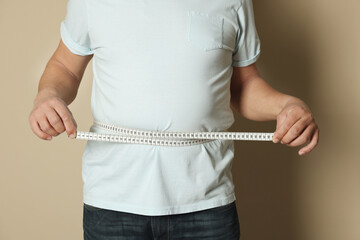 Man measuring waist with tape on beige background, closeup