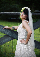Modern Edgy And Funky Country Bride With Neon And Black Hair.  Side View Showing Veil And Back Of Wedding Gown -- Brides Arm On Fence And Shows A Star Wars Stormtrooper Forearm Tattoo.