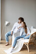 Young beautiful couple at home in a cozy armchair, wear jeans and white shirts