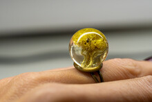 Dwarf Everlast Ring On A Finger. Sphere Ball Made Of Epoxy Resin With Natural Dried Flowers Inside. Selective Focus On The Details, Blurred Background.