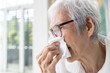 Asian senior woman sneezing in tissue paper having allergy to dust in her home,old elderly with allergic rhinitis,chronic rhinitis,hay fever,inflammation,nasal cavity,sinusitis,dust allergy concept.