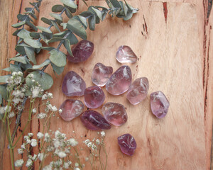 amethyst purple crystal tumbled semi precious stone, senitransparent rock, on raw natural wood with leaves and flowers babies breath