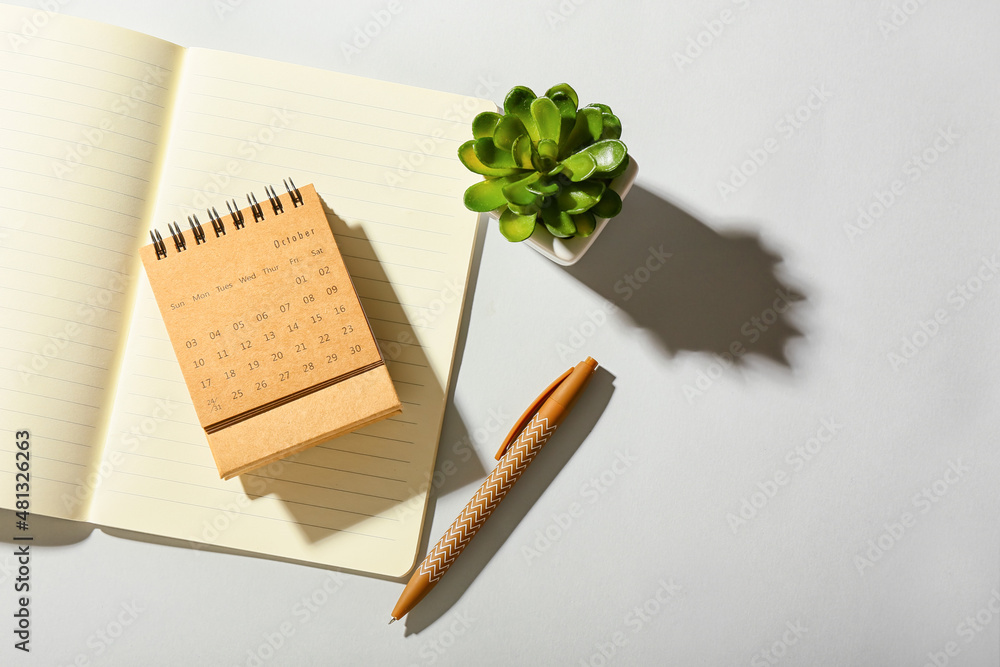 Craft calendar, notebook and houseplant on light background