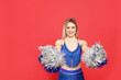 Beautiful cheerleader in costume holding pom poms on red background. Space for text
