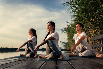 Group of people doing yoga exercises by the lake at sunset.