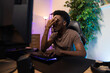 © ABCreative - Professional pro video gamer playing on computer lost round in the game, he is heartbroken, disappointed, ashamed, the man covers face with hand, the room lit with led neon lights