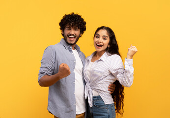 Big win. Happy indian couple celebrating success with raised fists, excited man and woman exclaiming with joy