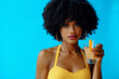 © Carlos David - beautiful young African American woman in bright summer outfit drinking refreshing cocktail isolated on blue background