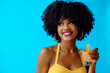 © Carlos David - beautiful young African American woman in bright summer outfit drinking refreshing cocktail isolated on blue background