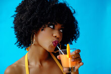 Beautiful Young African American Woman In Bright Summer Outfit Drinking Refreshing Cocktail Isolated On Blue Background