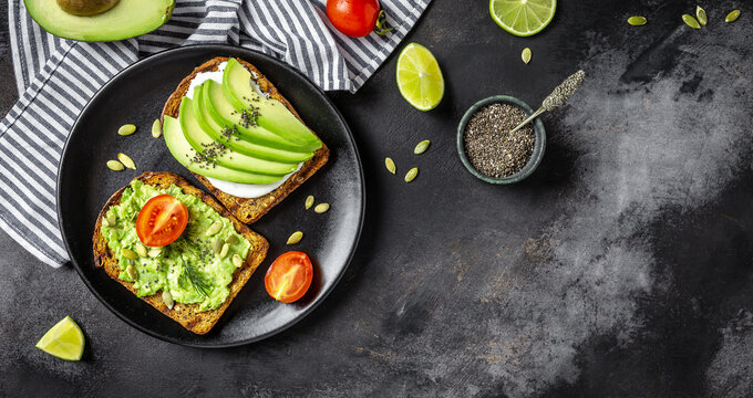 Healthy avocado toasts for breakfast or lunch with rye bread, cream cheese, arugula, sliced avocado, pumpkin, hemp and sesame seeds, salt and pepper. Vegetarian food concept. Clean eating. Top view