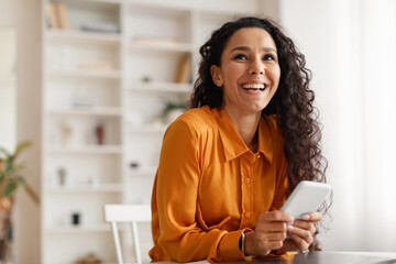 happy middle eastern lady using smartphone sitting at desk indoor