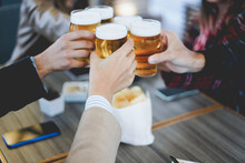 Group Of People Having Fun Cheering With Beer Inside Brewery Bar - Focus On Front Hand Holding Beer