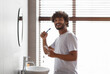 © Prostock-studio - Oral care concept. Happy bearded indian guy in white t-shirt brushing teeth with paste, smiling at camera in bathroom