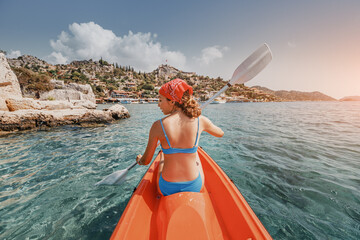 Wall Mural - Happy girl is rowing on a sea kayak near Kekova island with view of Simena Castle and Kaleucagiz village in Turkey. Outdoor recreation and exploration. Travel as a lifestyle