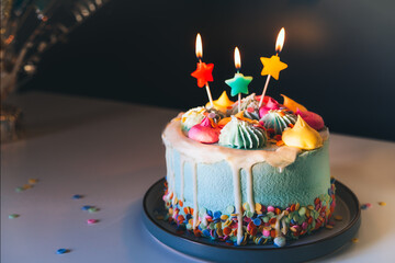 Colorful birthday cake with sprinkles and burning star shaped candles on a dark wall background. Festive birthday celebration, party. Selective focus, copy space