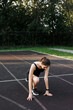 © Anna - A fitness woman doing a stretching exercise stretches her legs. Women stretch to warm up before running or training. In the park, on the sports field. side view, yoga elements.
