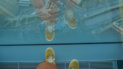 Wall Mural - Top view on man's feet in yellow leather sneakers. Man stands near panoramic window on high floor of building. Urban fashion of millennials.