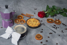 Cup With Black Coffee, Coffee Pot With Coffee Beans, Dried Oranges, Apple Pie, Cinnamon Stick And Red Rose On A Brown Background.