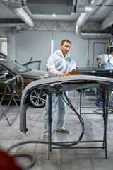 Serviceman polishing car body part in workshop